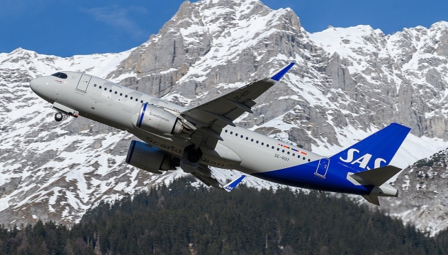 A SAS Airbus A320neo aircraft climbs into the air with a mountain in the background and a blue sky above
