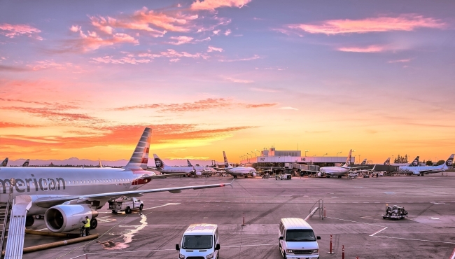 An american airlines jet on the ground at an airport surrounded by vehicles, with an orange sky in the background